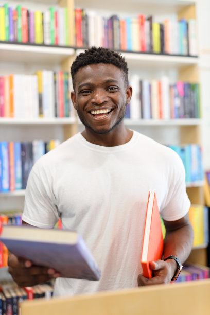 快乐的男生学生手里拿着一本书在图书馆。图片下载