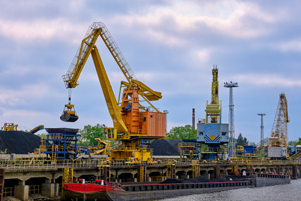 多云天，内河港口起重机带翻盖或抓手将煤炭装载到内河拖船或驳船。能源、矿产、环境图片下载