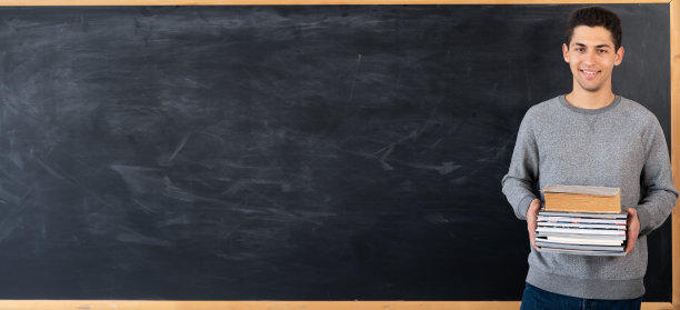 年轻的阿拉伯老师站着用书本做黑板背景，大学生拿着课本靠近黑板，在教室里打着学习和教育理念的横幅图片下载