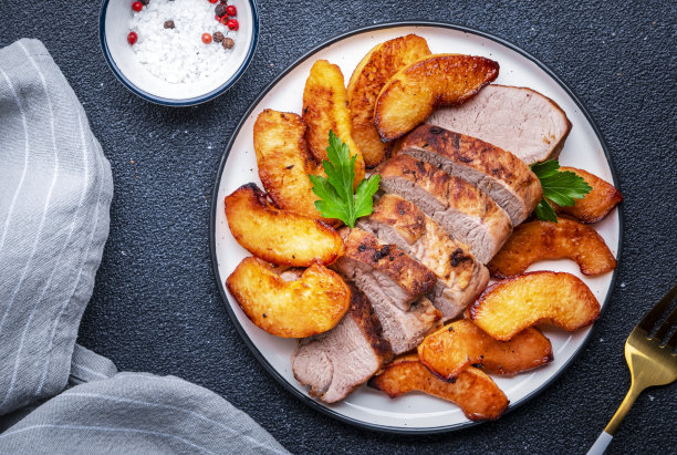 烤猪里脊配甜榅桲或苹果片，白色盘子。黑色表格背景，俯视图图片下载