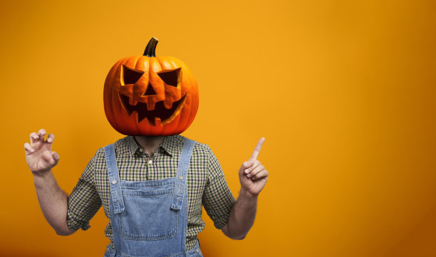 可怕的人在万圣节稻草人服装与南瓜灯南瓜头指向橙色背景与复制空间图片下载