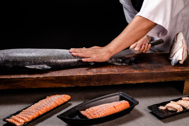 厨师的手握着新鲜的三文鱼。厨师准备日本食物的特写镜头。日本厨师在餐厅做寿司。厨师在木板上制作传统的日本寿司。图片下载