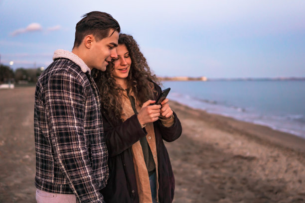 一对年轻夫妇在海滩上使用手机图片下载