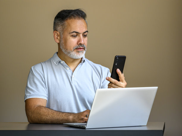 一个成熟的商人拿着笔记本电脑看着他的手机图片下载