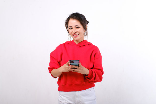 微笑的亚洲女性，身穿红色毛衣和白色裤子，手持智能手机图片下载