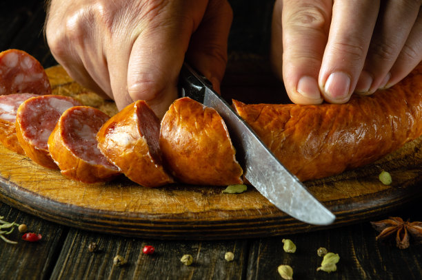 厨师用刀在砧板上切香肠的特写镜头。烹饪快餐或三明治的概念图片下载