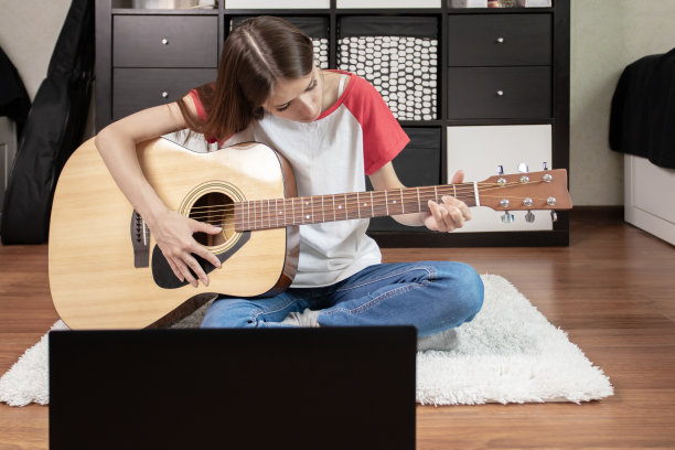 一个十几岁的女孩，拿着一把原声吉他和一台笔记本电脑，在她的房间里享受着她对音乐的热情图片下载