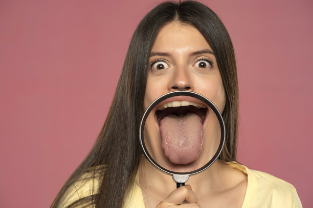 年轻快乐的女人通过放大镜展示她健康的舌头图片下载