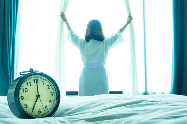新的一天的早晨，闹钟叫醒了坐在房间里的女人。一位妇女在窗口伸展肌肉。健康和护理概念图片下载