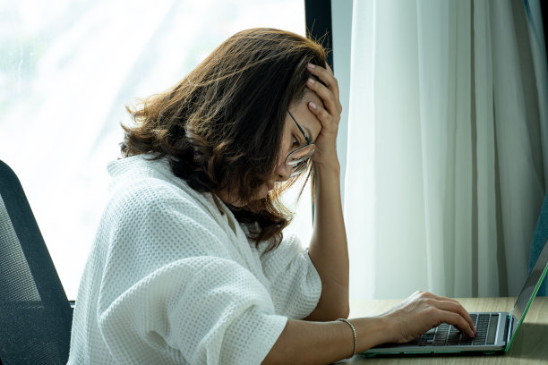 女人坐下来，他的脸不安。在电脑桌前，她感到头痛和压力。因为工作辛苦，休息不足。图片下载