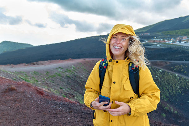 徒步旅行在欧洲大陆最高的火山-埃特纳。身穿黄色雨衣的年轻女子微笑着站在埃特纳火山全景的山顶上。图片下载