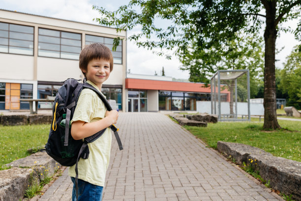 一个男孩背着背包从学校走出来。孩子们上学，享受学年的开始或结束。图片下载