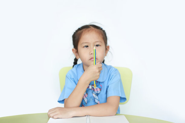 穿着校服的小女孩手里拿着铅笔，看着白色背景上的铅笔。一边学习一边思考的小女孩。图片下载