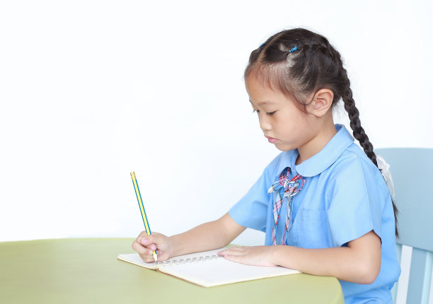 打算穿校服的小女孩在白底孤立的书桌上写笔记本。图片下载