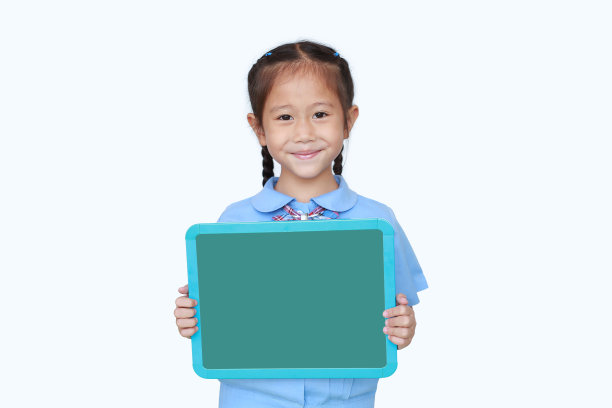 穿着校服的开朗的亚洲小女孩在白色的背景上拿着白板。孩子拿着绿色的空黑板。教育和学校理念。图片下载