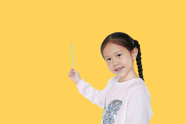 肖像小亚洲儿童女孩站着，指着在黄色的背景与复制空间孤立的东西。教育观念中的亚洲女学生。图片下载