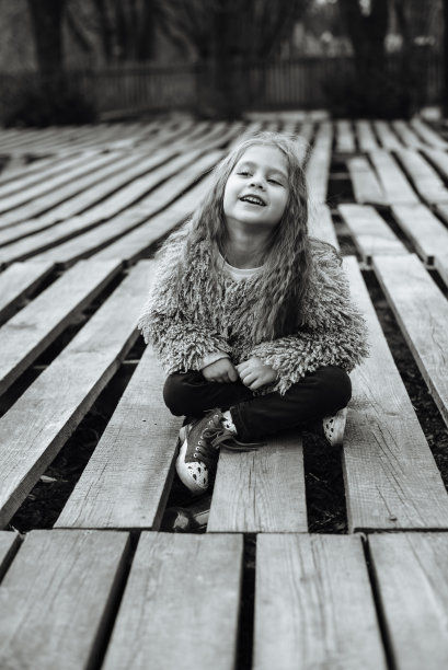 小可爱的女孩肖像与长卷发。在室外的花园里。时髦的学龄前儿童坐在公园里的木托盘上。文本。黑白照片图片下载