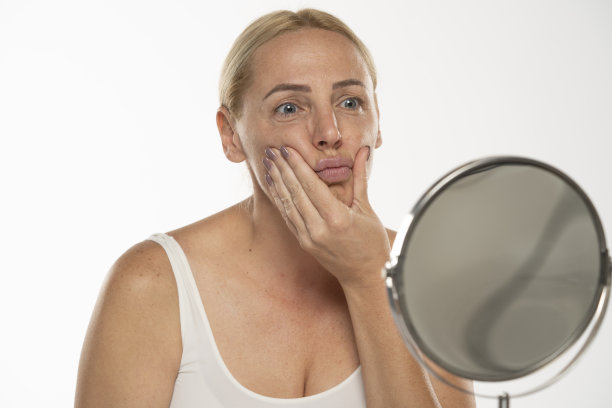 镜子前忧心忡忡的金发中年女子在白底上摸了摸自己的嘴。图片下载