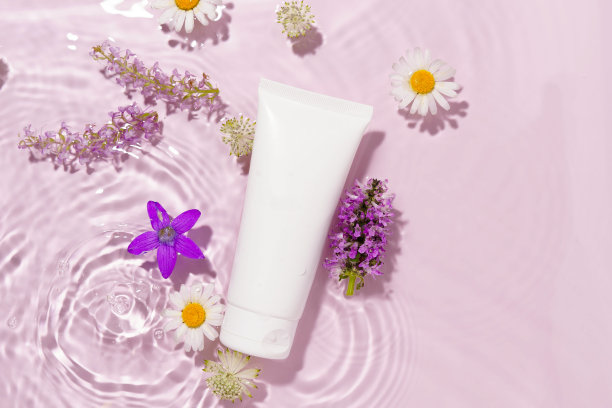 白色面部润肤霜管模型在水的纹理与波浪和花朵在粉红色的背景。天然护肤化妆品的概念。图片为您的设计图片下载