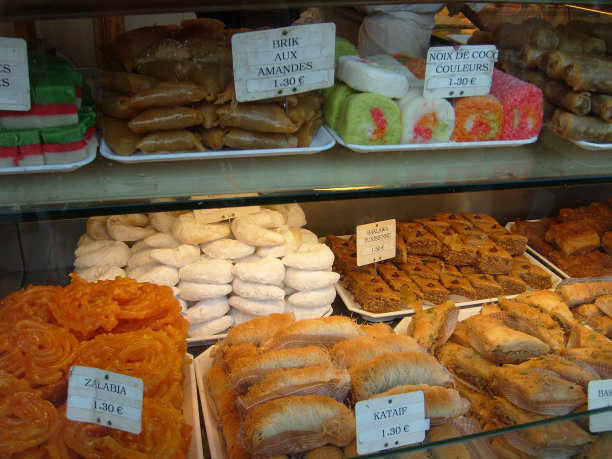 肉饼、蛋糕、卷饼和糖果放在柜台上，柜台后面的玻璃展柜向顾客出售。价格标签以欧元表示。烹饪产品放在托盘上。法国的美食。粉甜甜圈图片下载
