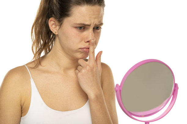 年轻的不快乐的女人用手指在一个白色的背景上触摸她的鼻子图片下载