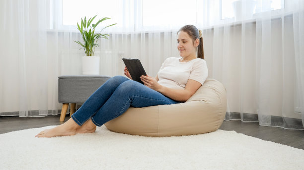 美丽的微笑的女人在家里的平板电脑上工作在客厅的大窗户图片下载