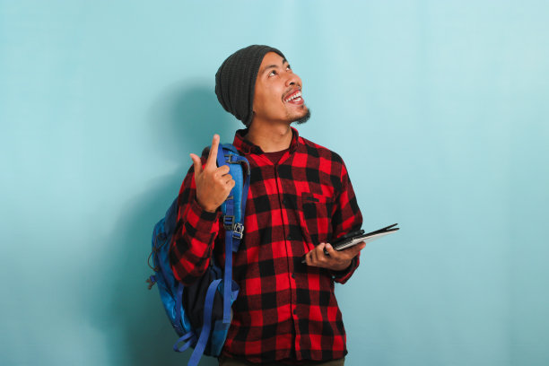 一个兴奋的亚洲年轻人拿着一本书，站在蓝色的背景下，手指着上面图片下载