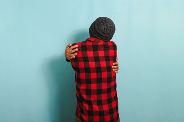 年轻的亚洲男子站在蓝色背景下拥抱自己。自爱和自我照顾的概念图片下载