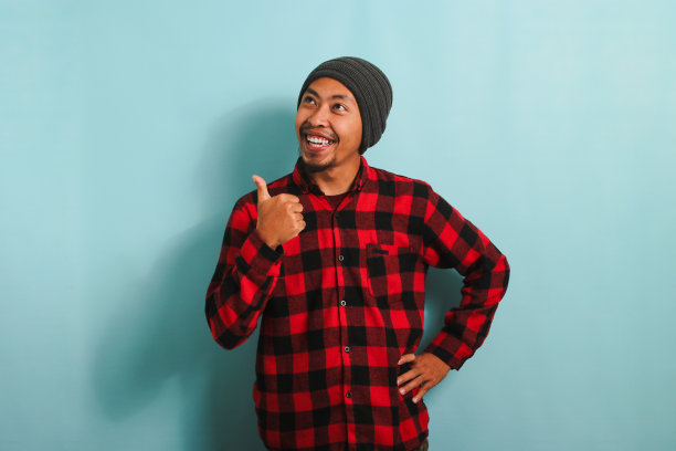 年轻的亚洲人正用手指着旁边空荡荡的拷贝空间，孤立在蓝色的背景上图片下载