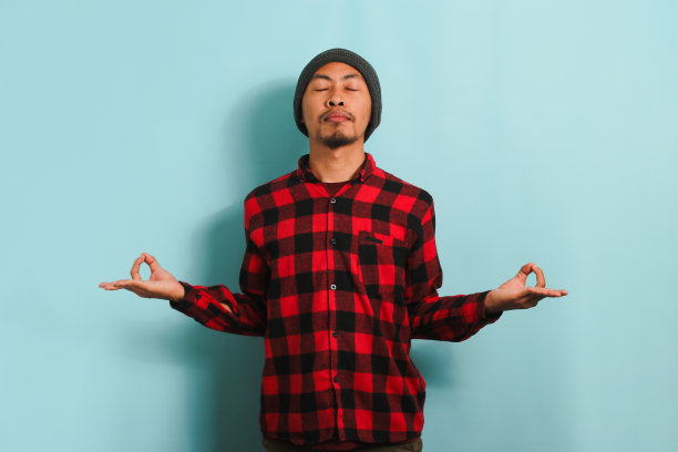 一个冷静的亚洲年轻人正站在蓝色背景下冥想和练习瑜伽图片下载