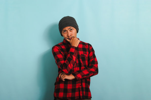 忧郁的年轻亚洲人把手放在下巴上，看起来很严肃，在蓝色背景中显得很孤立图片下载