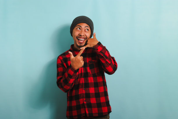 兴奋的年轻亚洲男子做叫我的手势，指着右边，孤立的蓝色背景图片下载