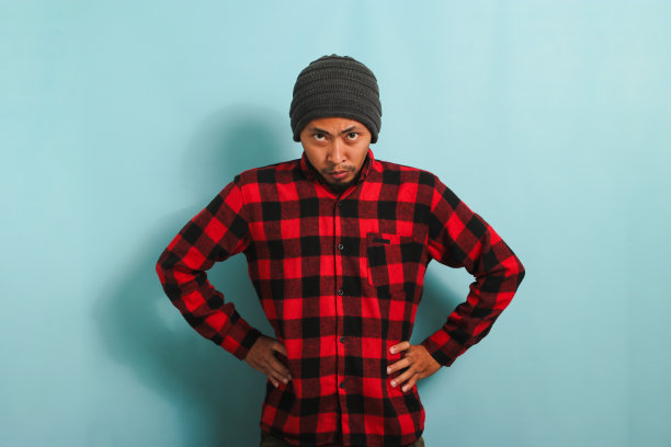 愤怒的年轻亚洲男子两手叉腰站着，盯着镜头，孤立在蓝色背景中图片下载