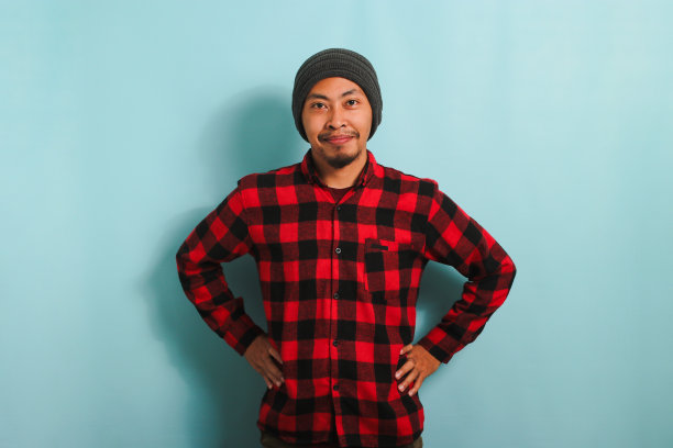 快乐的年轻亚洲男子保持手臂在腰部叉腰的姿势，站在蓝色的背景图片下载