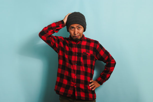 一个不开心的亚洲年轻人站在蓝色的背景下，抓着自己的头，感到焦虑图片下载