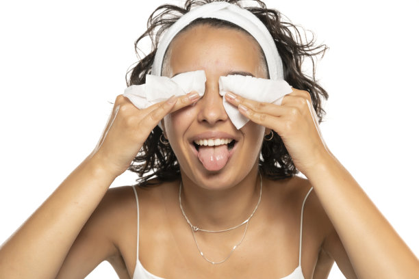 一个年轻有趣的黑发女人用湿巾洗脸的画像。在白色的摄影棚背景下，女孩正在用面巾纸卸妆。图片下载