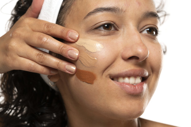 黑皮肤的女人的脸与三种不同色调的液体粉底在一个白色的背景图片下载