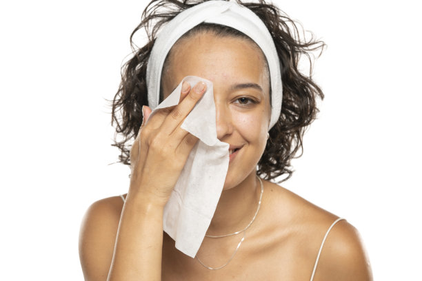 一个年轻的黑发女子用湿巾洗脸的画像。在白色的摄影棚背景下，女孩正在用面巾纸卸妆。图片下载