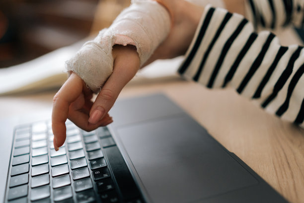 特写镜头显示，无法辨认的受伤年轻女商人右手受伤，用白色石膏绷带包裹着，正在笔记本电脑上打字图片下载