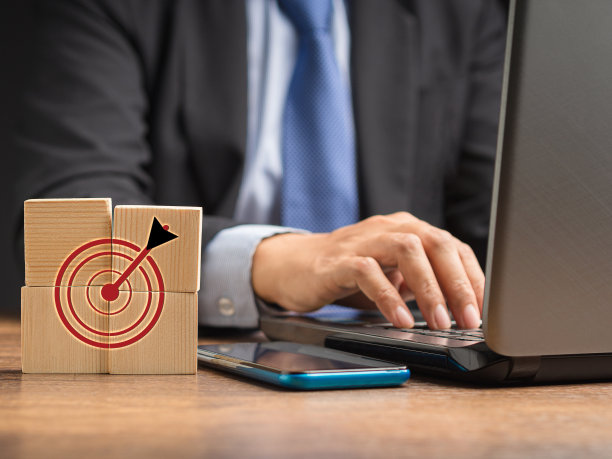 飞镖瞄准瞄准图标在桌子上的木制立方体与商人使用笔记本电脑在办公室图片下载
