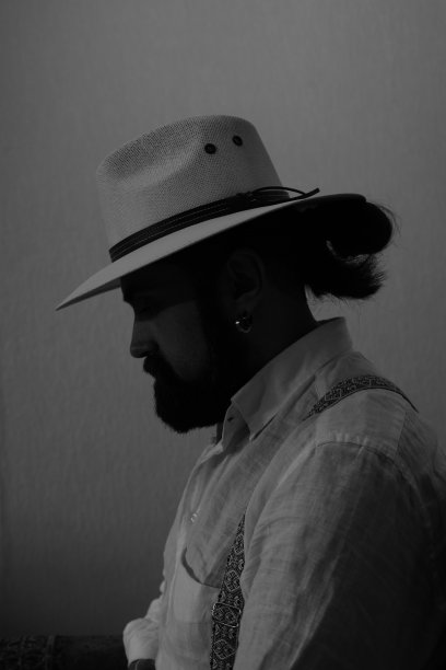 一个穿着白衬衫、戴着白帽子、留着胡子的时髦男人坐在一把老式椅子上。图片下载