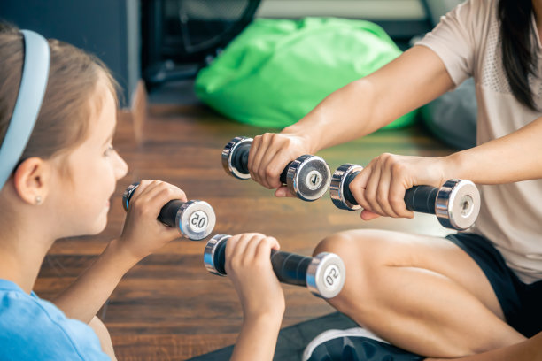 一位妇女带着女儿在健身房的地板上用哑铃做运动。图片下载