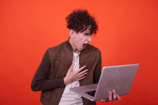 拿着笔记本电脑摆出橙色背景的搞笑人。图片下载