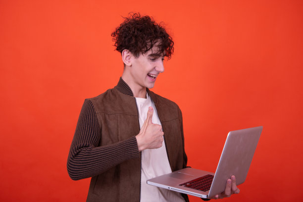 拿着笔记本电脑摆出橙色背景的搞笑人。图片下载