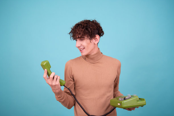 一位年轻英俊的男子对着一部旧电话讲话。图片下载