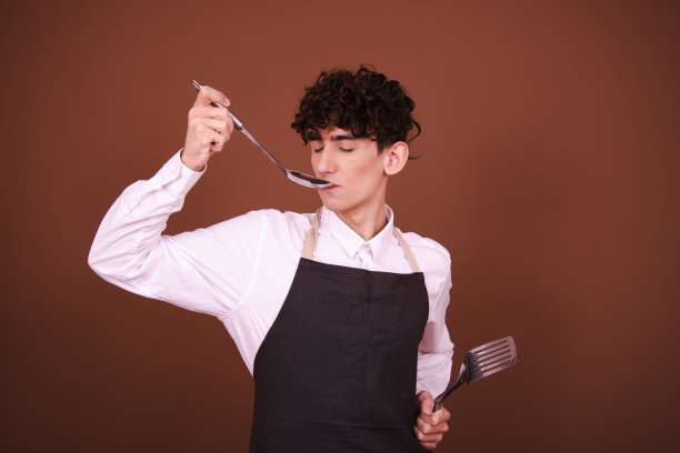 拿着金属勺子的年轻有趣的厨师。图片下载