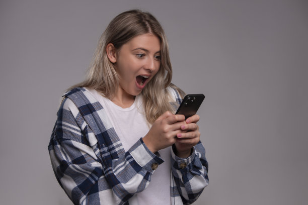 惊讶的年轻女子被孤立在灰色背景中使用手机图片下载