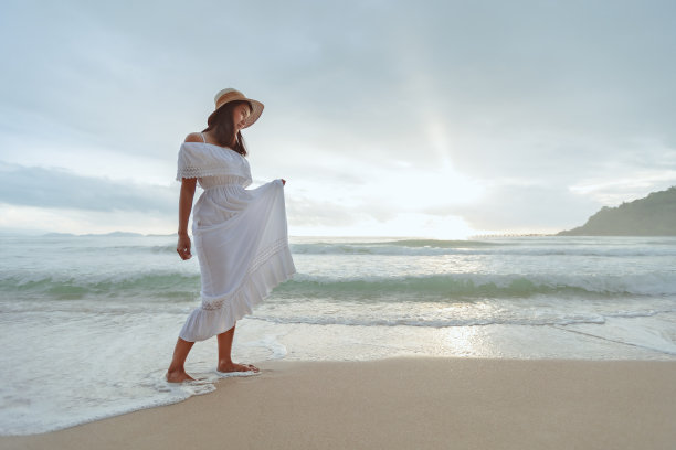 亚洲女人戴着时髦的帽子和衣服走在沙滩上，享受美丽的大自然在日落的时间。图片下载
