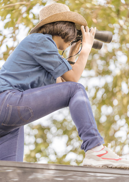 草地上戴着帽子拿着双筒望远镜的女人图片下载