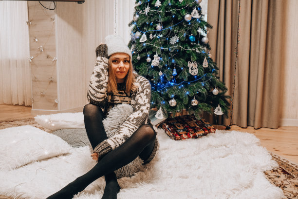 漂亮的年轻女孩坐在圣诞树旁边。新年装饰。家庭内部。寒假图片下载